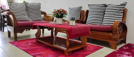 A living room with a wooden sofa, striped pillows, a red table, and a floral rug.