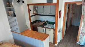 Una cocina compacta con encimera de madera, un lavamanos y armarios. Hay una mesa de comedor con un cuenco de fruta.