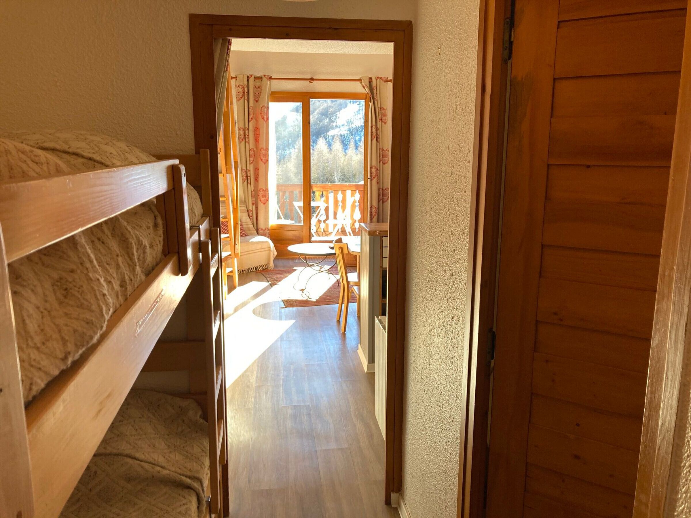 A wooden interior with a bunk bed, a small table, and a view of the outdoors through a window.