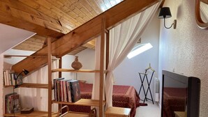 Un dormitorio acogedor en el ático con vigas de madera, techo inclinado, una estantería, un televisor y una cama con ropa de cama estampada.