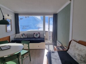 Une pièce dotée d’un balcon, d’un canapé, d’une table à manger avec des chaises et d’une fenêtre donnant sur un paysage enneigé.