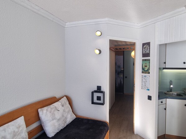 A compact room with a bed, a small kitchenette, and a hallway leading to another room.