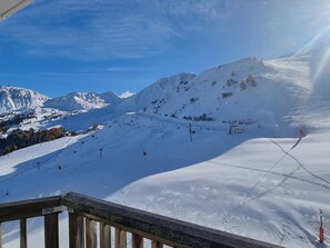 Un paysage montagneux enneigé avec des pistes de ski, un télésiège et une rambarde en bois au premier plan.
