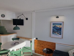 A room with a dining table, chairs, a television, a framed picture, and a bunk bed.