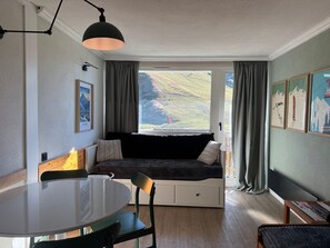 Een knus vertrek met een groot raam, een eettafel en een comfortabele zithoek.