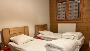 A room with two wooden beds, white bedding, a window with heart-patterned curtains, and a radiator. - Cozy T3 apartment near center with terrace and parking (Samoëns)