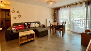 A cozy living room with a sectional sofa, a wooden coffee table, and a dining area with a table and chairs. - Cozy T3 apartment near center with terrace and parking (Samoëns)