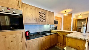 A kitchen with wooden cabinets, a black stove, a sink, and a microwave. - Cozy T3 apartment near center with terrace and parking (Samoëns)