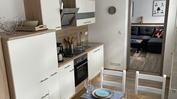 Una cocina compacta con muebles blancos, una encimera de madera y un comedor con mesa de madera y sillas blancas.