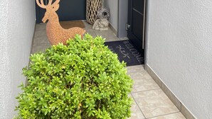 Una entrada moderna con un ciervo decorativo, un pequeño arbusto y un felpudo de bienvenida.
