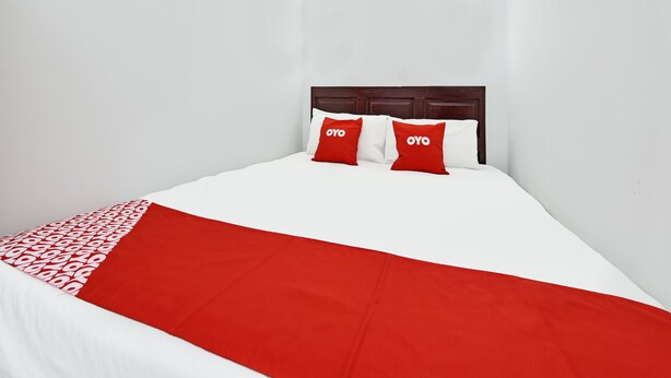 Una cama bien hecha con una colcha blanca y roja, dos almohadas rojas con un logotipo y un cabecero de madera.