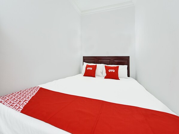 Una cama bien hecha con una colcha blanca y roja, dos almohadas rojas con un logotipo y un cabecero de madera.