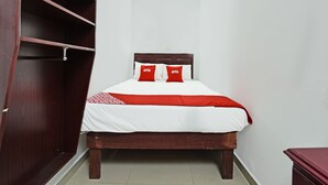 Una cama bien hecha con ropa blanca y roja, un cabecero de madera y una almohada roja y blanca con el texto "OYO".
