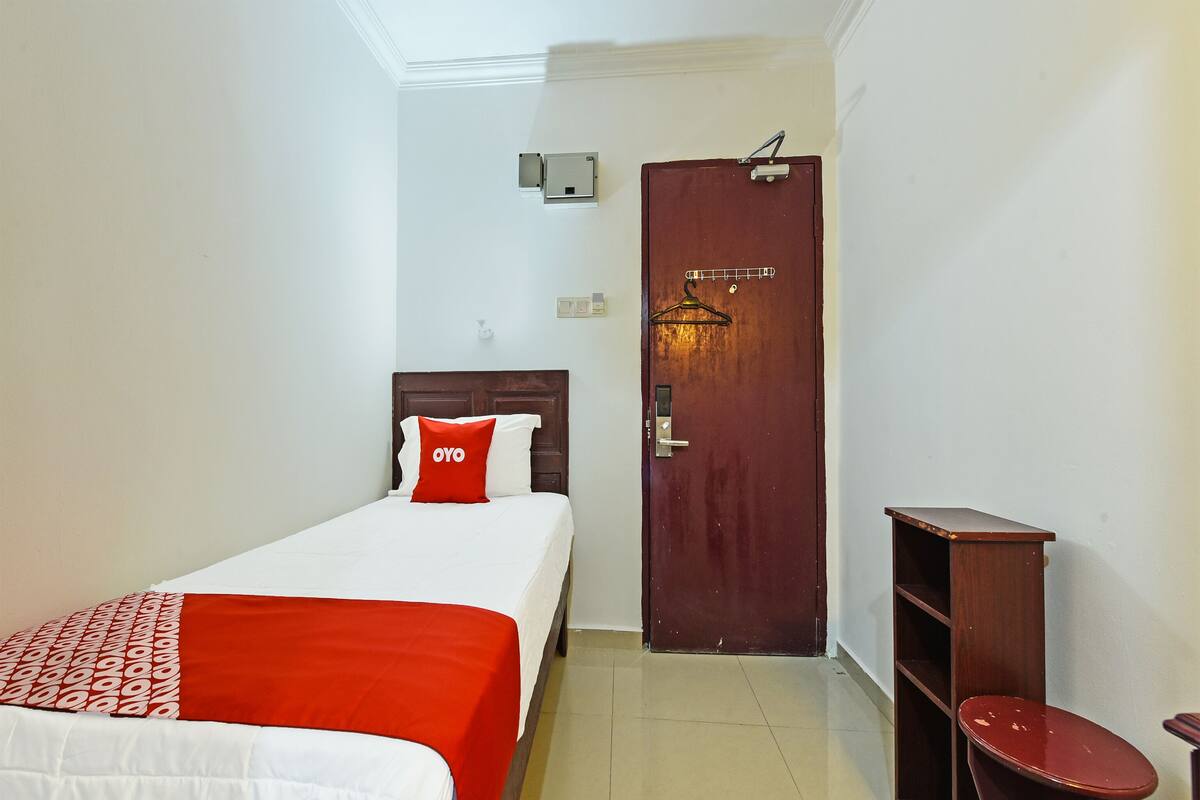 Una habitación de hotel con una cama, una puerta de madera, una mesita pequeña y una silla.