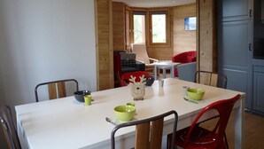 Uma sala de jantar com uma mesa branca, cadeiras vermelhas e cinzentas, e uma janela com moldura de madeira.