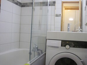A bathroom with a glass shower enclosure, a white bathtub, and a front-loading washing machine.