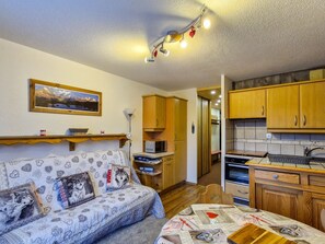 Um quarto acolhedor com sofá, mesa de jantar, armários de madeira, micro-ondas e um quadro na parede.