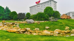 A building with a large red flower on top, surrounded by a grassy area with rocks and trees. - Daohuaxiang Hotel (Yichang)