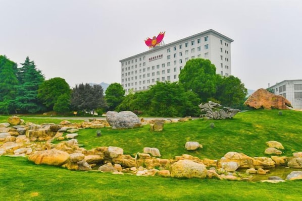 A building with a large red flower on top, surrounded by a grassy area with rocks and trees.