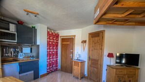 A compact kitchen with a microwave, kettle, and utensils. There is a wooden table and a TV in a corner.