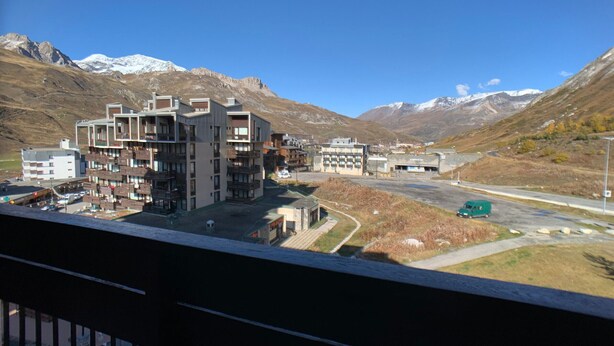 A modern multi-story hotel with balconies, a parking area, and a view of snow-capped mountains.