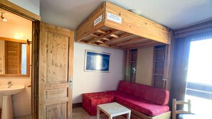A rustic cabin interior with a wooden ceiling, a red sofa, a small table, a wooden bench, and a white sink.
