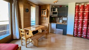A cozy cabin interior with a wooden dining table, chairs, a bench, a kitchen area with a microwave, refrigerator, and utensils.