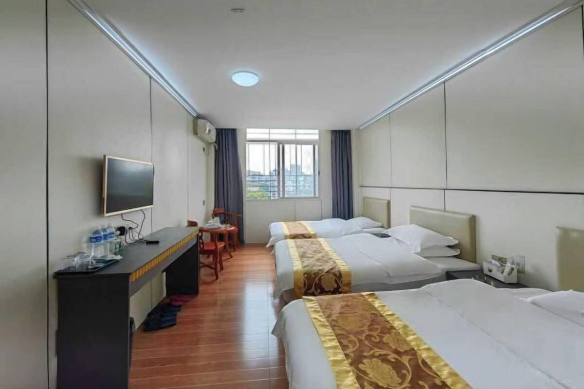 A hotel room with two beds, a desk with a chair, a television, and a window with curtains.