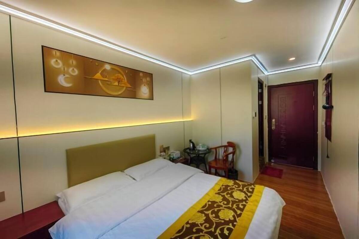 A hotel room with a bed, a wall-mounted artwork, a small table with a chair, and a door.