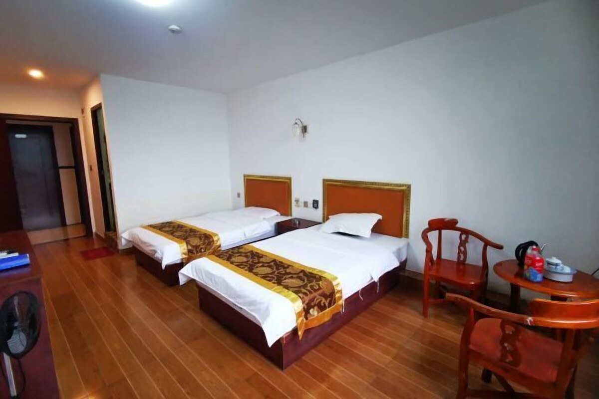 Habitación de hotel con dos camas, suelo de madera, un escritorio y una mesita con una silla.