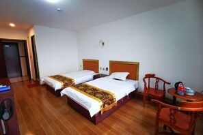 Habitación de hotel con dos camas, suelo de madera, un escritorio y una mesita con una silla.