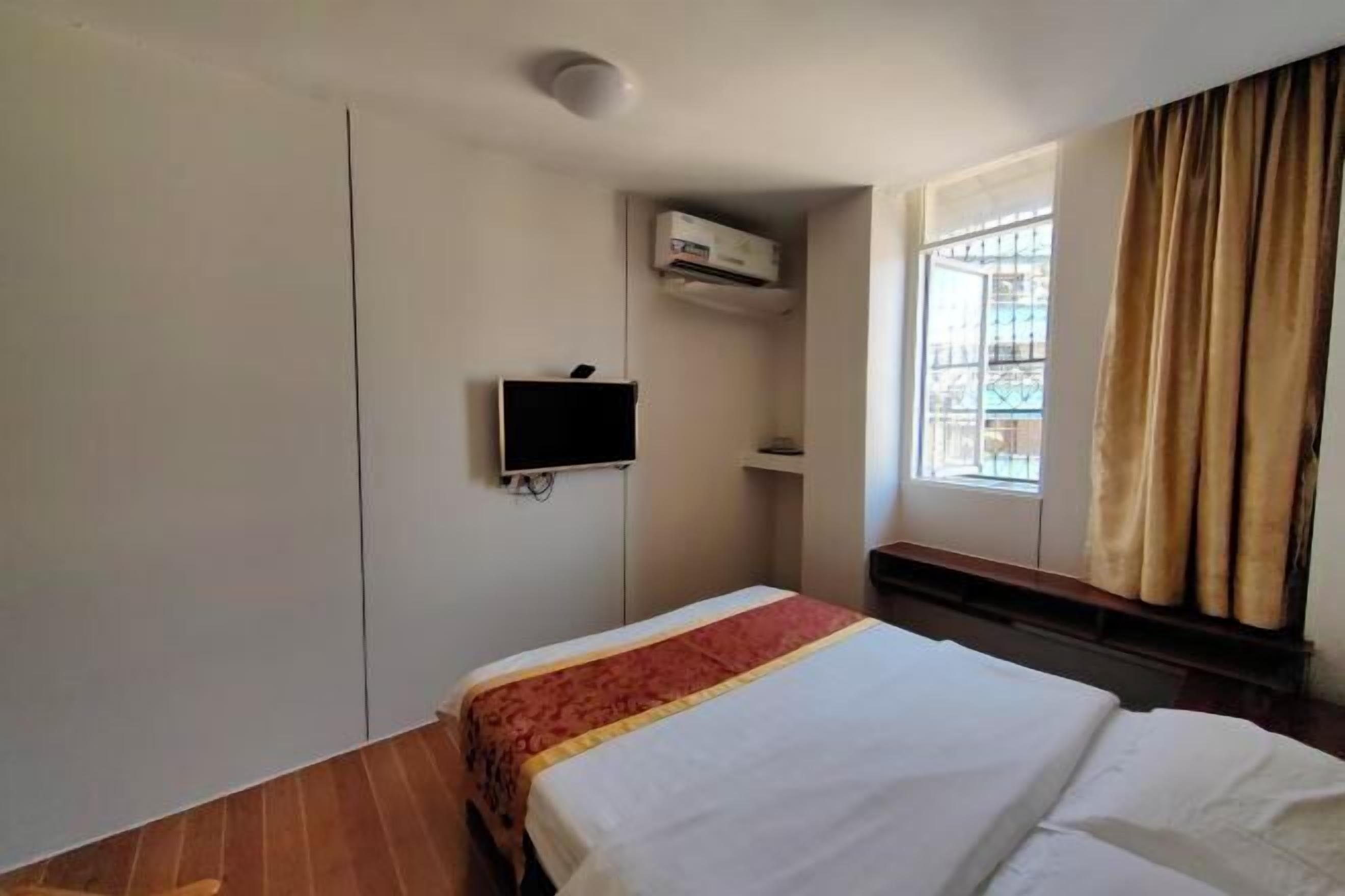 A hotel room with a bed, a TV, an air conditioning unit, and a window with curtains.