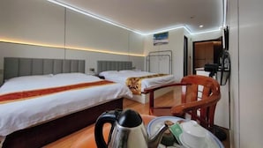 Habitación de hotel con dos camas, una silla de madera, un hervidor y una mesita con una taza y un plato.