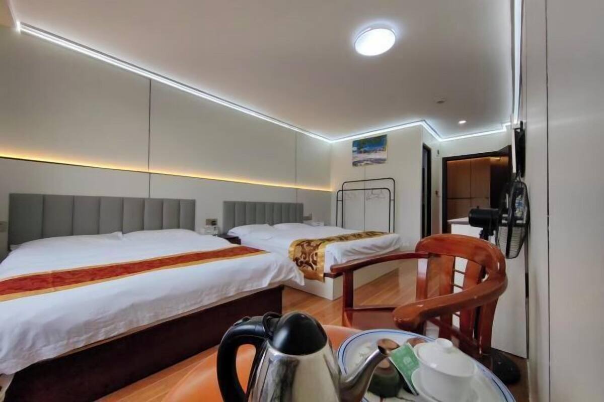 A hotel room with two beds, a wooden chair, a kettle, and a small table with a cup and saucer.