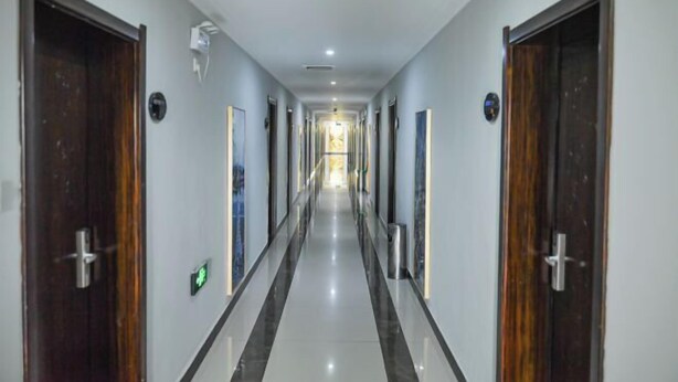 Un pasillo largo y estrecho con puertas a ambos lados, que conduce a una habitación luminosa al final.