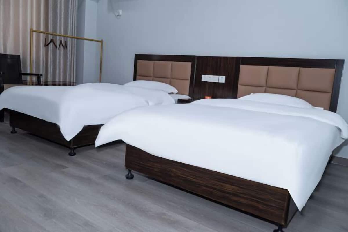 Une chambre d’hôtel avec deux lits, chacun doté d’un cadre et d’une tête de lit en bois, et un sol gris.