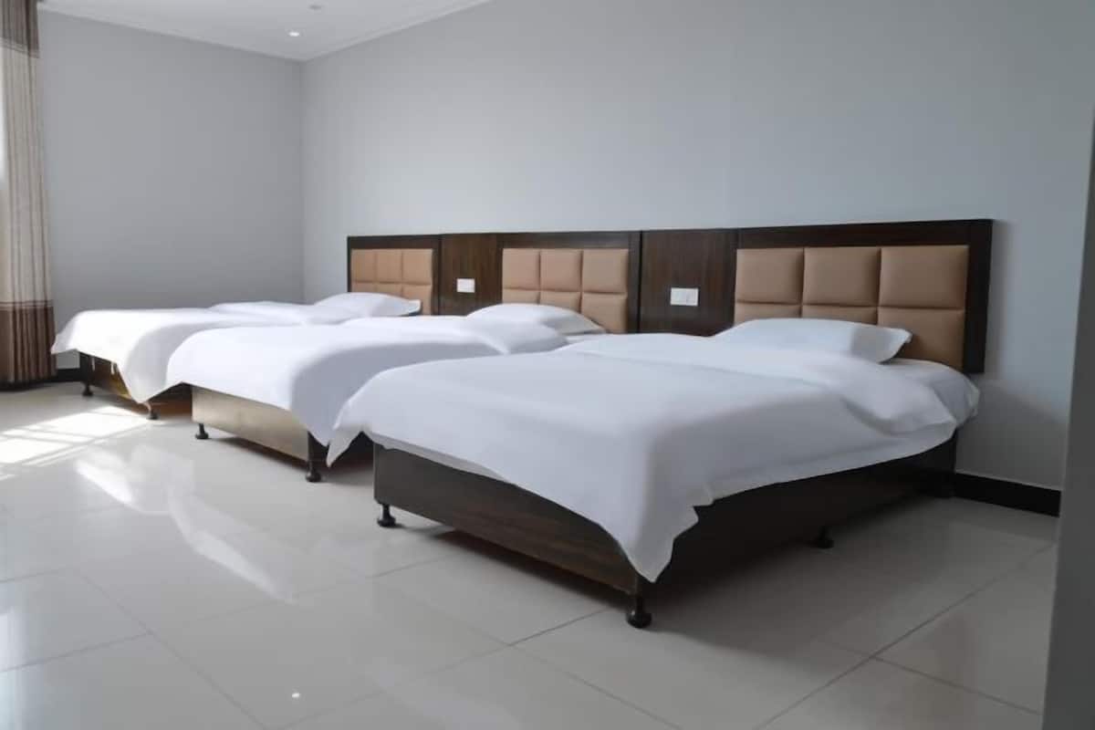 Une chambre d’hôtel avec trois lits simples, chacun doté d’une tête de lit en bois et de draps blancs.
