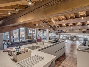 A spacious kitchen with a large island, wooden beams, and large windows.