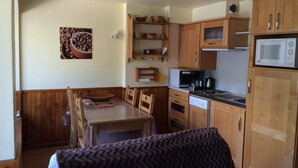 Une cuisine compacte dotée de meubles en bois, d’un four à micro-ondes, d’une machine à café et d’un coin repas avec une table et des chaises.