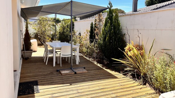 A patio area with a table and chairs, a wooden deck, and a shaded umbrella. - Bright house villa (Andernos-les-Bains)