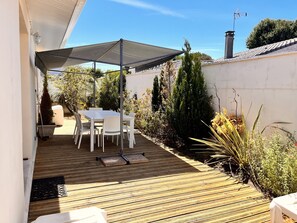 Un espace extérieur aménagé avec une table et des chaises, une terrasse en bois et un parasol pour créer de l’ombre.