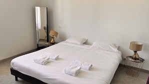 A neatly made bed with white linens and towels, a bedside table with a lamp, and a mirror on the wall. - Bright house villa (Andernos-les-Bains)