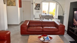 A living room with a red leather sofa, a wooden coffee table with magazines, a TV, and a dining area with a table and chairs. - Bright house villa (Andernos-les-Bains)