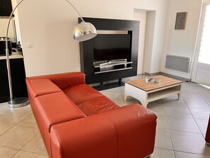 Un salon moderne avec un canapé en cuir rouge, une table basse en bois et un meuble de rangement noir intégrant un téléviseur.