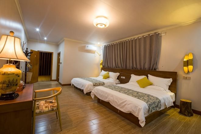 Habitación de hotel con dos camas, un escritorio con lámpara, una silla, piso de madera y una lámpara en el techo.