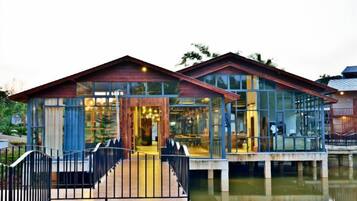 A waterfront property with a glass-enclosed building, a wooden deck, and a metal railing.
