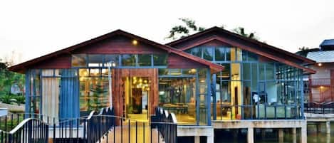 A waterfront property with a glass-enclosed building, a wooden deck, and a metal railing.
