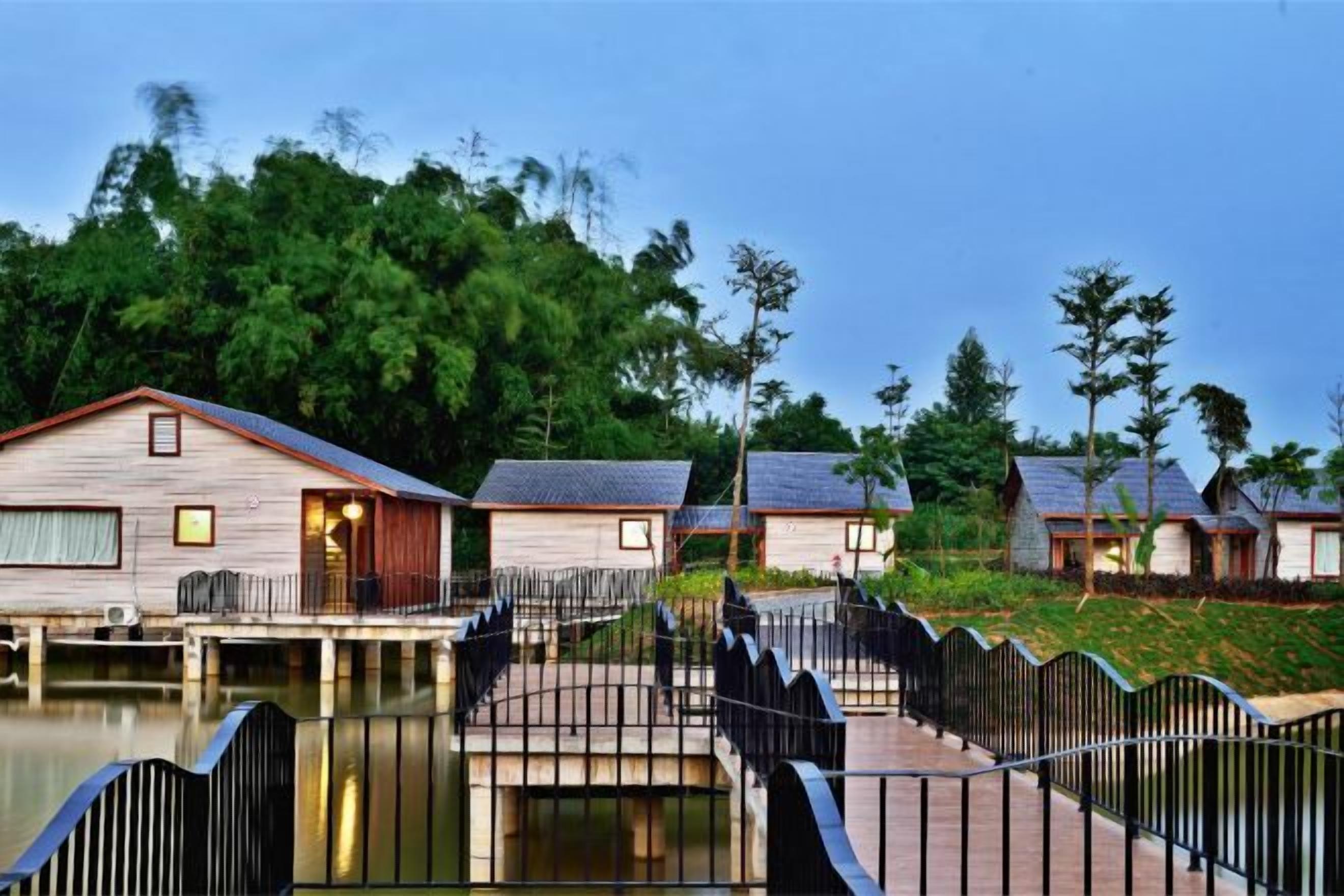 A row of wooden cabins with a bridge connecting them over a body of water, surrounded by greenery.
