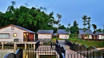 A row of wooden cabins with a bridge connecting them over a body of water, surrounded by greenery.