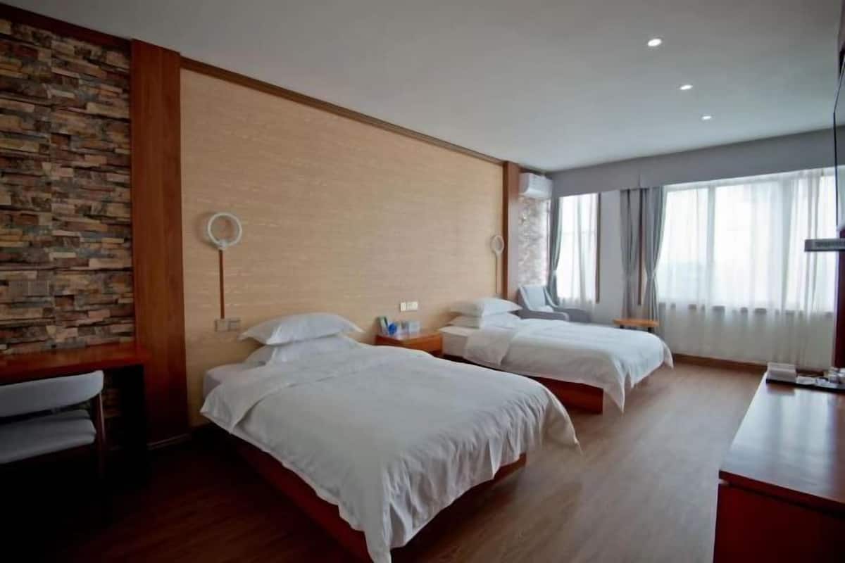 Ett hotellrum med två sängar, ett trägolv, en vägg av sten och ett stort fönster med gardiner.